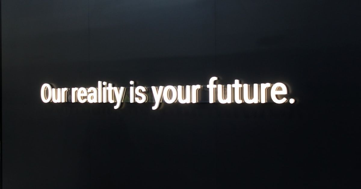 a black wall with a neon sign that says our reality is your future