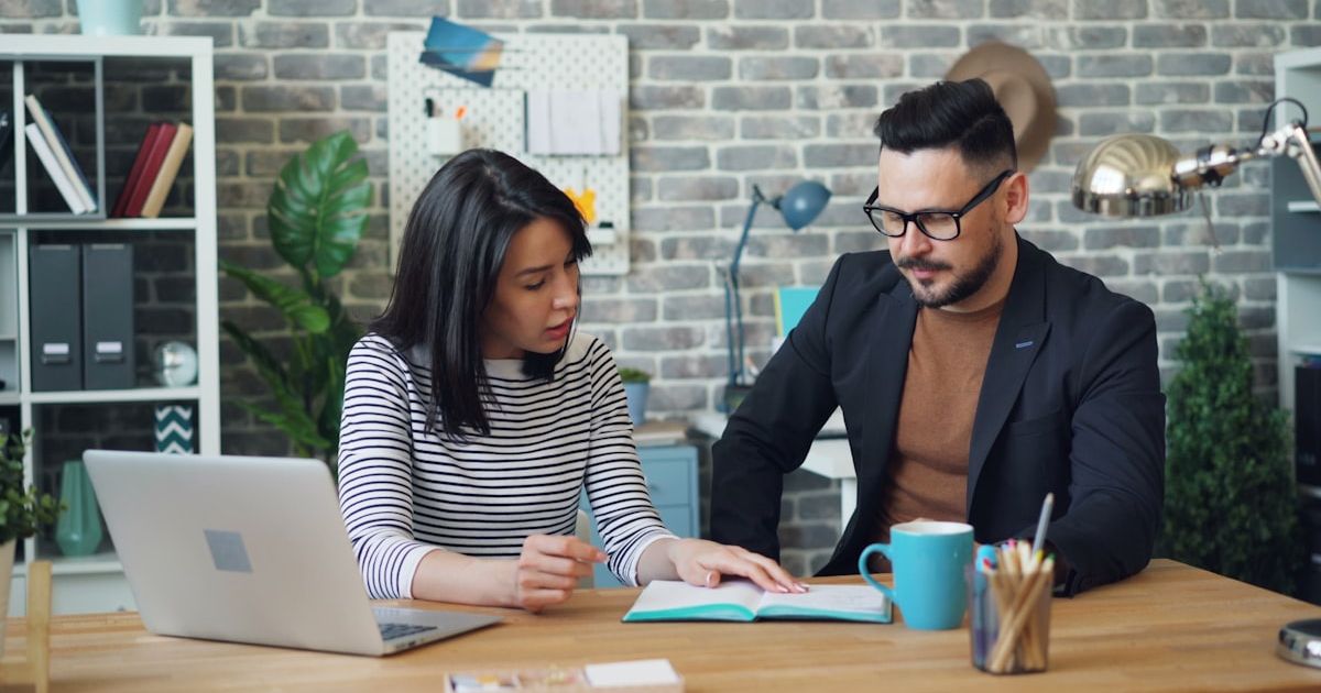 a man and a woman sitting at a table looking at a laptop